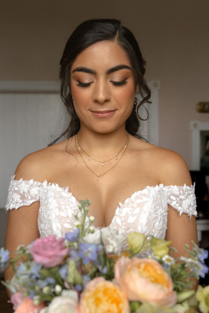 Bride with long lashes looking down at her colorful bouquet she is being photographed by a Charlotte wedding photographer