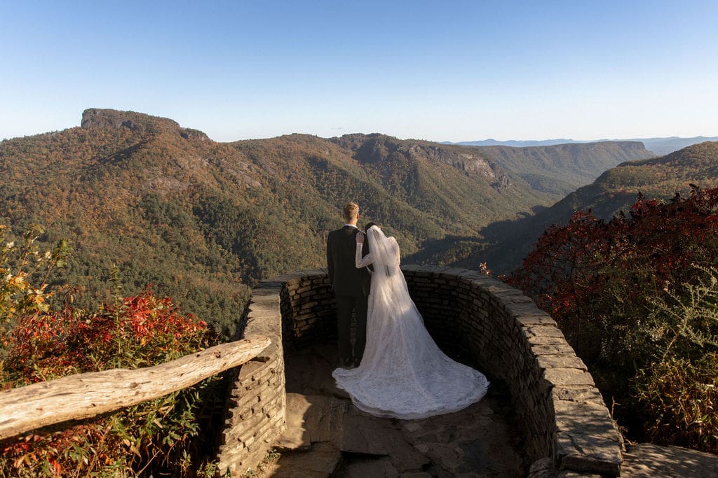 Bride and groom overlooking fall foliage from a stone overlook during NC mountain elopement in Western North Carolina